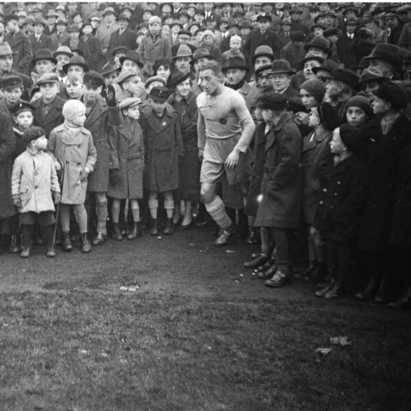 Die Zuschauer in der Kampfbahn Glückauf stehen bis zum Rand des Spielfelds. Zwischen ihnen läuft der Spieler des FC Schalke 04 Adolf Urban an, um einen Eckball zu schießen.