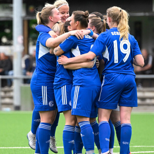 Fußballspielerinnen in Trikots vom FC Schalke 04 umarmen sich auf dem Spielfeld.