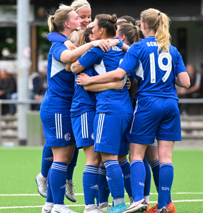 Fußballspielerinnen in Trikots vom FC Schalke 04 umarmen sich auf dem Spielfeld.
