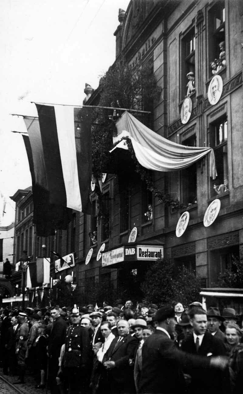 Eine Menschenmenge wartet am Schalker Markt vor der mit Fahnen geschmückten Kaiserhalle. An der Hausfassade hängen große Porträts der Spieler des FC Schalke 04.