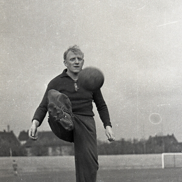 Fritz Szepan steht in langer Trainingskleidung auf dem Platz und sein rechtes Bein, um einen Fußball in der Luft anzunehmen.