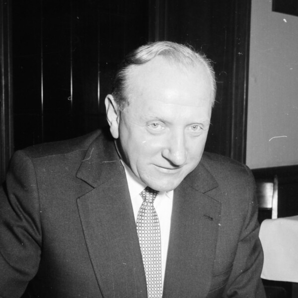 Fritz Szepan sitzt in einem Anzug und Krawatte an einem Tisch und füllt einen Wettschein aus. Unter dem Wettschein liegt eine aufgeschlagene Zeitung.