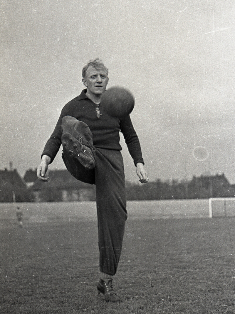 Fritz Szepan steht in langer Trainingskleidung auf dem Platz und sein rechtes Bein, um einen Fußball in der Luft anzunehmen.