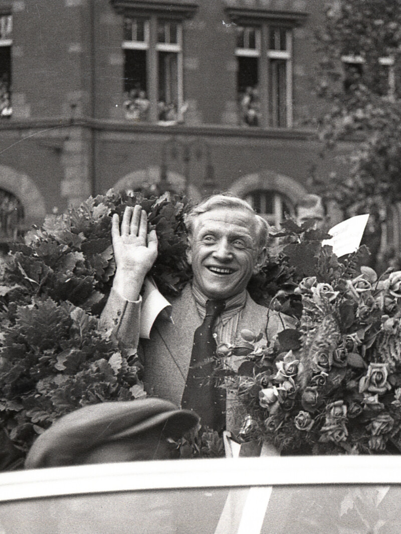 Fritz Szepan sitzt in einem offenen Wagen und wird bei der Feier zur Deutschen Meisterschaft 1939 durch Gelsenkirchen gefahren. Er lächelt und winkt den Zuschauern zu. Er trägt einen Siegeskranz um die Schultern und hält einen Blumenstrauß in der Hand.