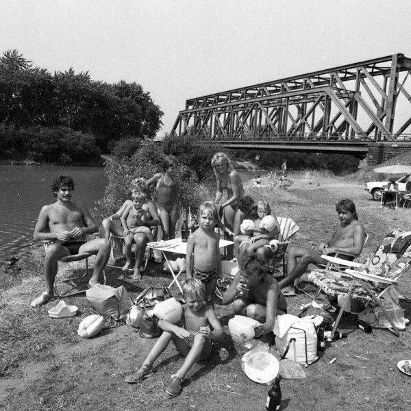 Zwei Familien sitzen mit ihren Kindern in Schwimmkleidung am Ufer des Rhein-Herne-Kanals um einen Campingtisch.