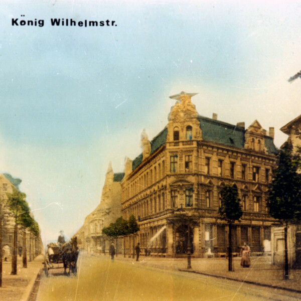 Eine Ansichtskarte der König-Wilhelm-Straße in Schalke um die Jahrhundertwende. Die Straße ist befestigt und gepflegt. Die Bürgersteige sind mit Bäumen bepflanzt.