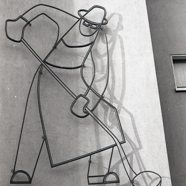 Auf einer Fassade sind die Umrisse eines Stahlarbeiters zu erkennen. Er trägt zum Schutz eine Schürze und Handschuhe. In den Händen hält er eine Gießkelle.