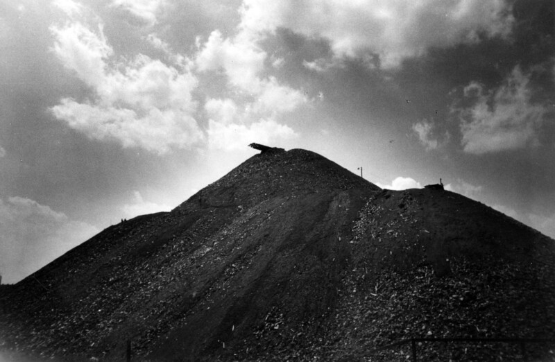 Die Fotografie zeigt eine Halde. Die Aufnahme wurde von unten aufgenommen. Die Halde wirkt massiv.