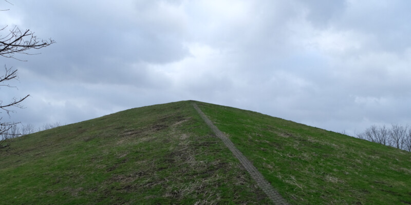 Eine kleine, mit Gras bewachsene Pyramide ragt in den bewölkten Himmel über Gelsenkirchen-Schalke.