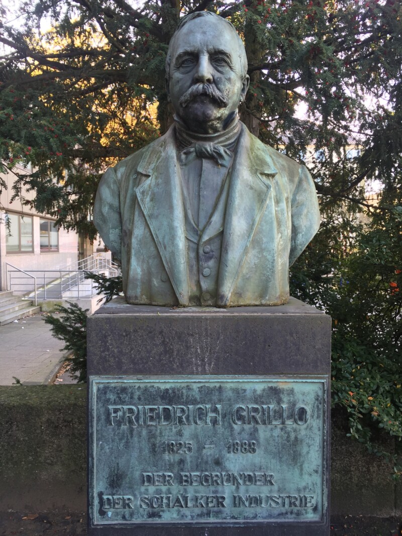 Nahaufnahme der Büste Friedrich Grillos auf dem Grilloplatz in Gelsenkirchen-Schalke. Auf dem Sockel ist ein Plakette mit der Aufschrift "Friedrich Grillo. Der Gründer der Schalker Industrie" angebracht.