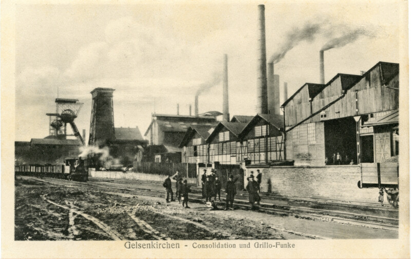 Eine Gruppe Männer steht vor den Industrieanlagen der Zeche Consolidation. Über den Gebäuden hinter ihnen ragen rauchende Schornsteine in die Luft. Links stehen die Fördertürme 1 und 6 der Zeche Consolidation.