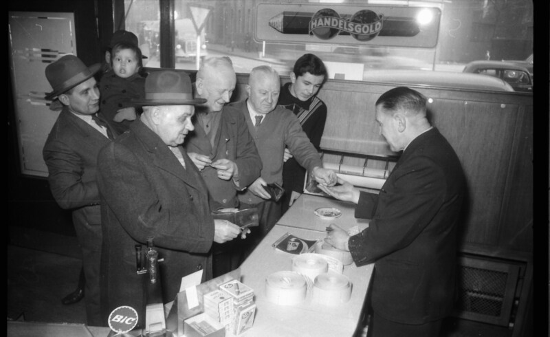 Ernst Kuzorra steht hinter der Ladentheke und kassiert fünf Kunden ab. Auf dem Tresen liegen Rollen mit Karten.