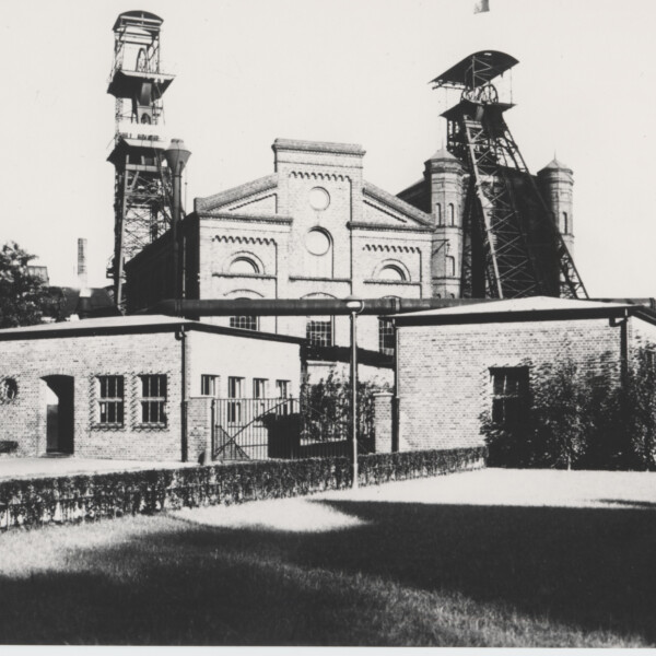 Im Vordergrund sind zwei flache, eingeschossige Gebäude zu sehen. Dahinter erhebt sich ein etwa doppelt so hohes Gebäude sowie die Fördergerüste von Schacht 3 und Schacht 4 der Zeche Consolidation im Stadtteil Gelsenkirchen-Bismarck.