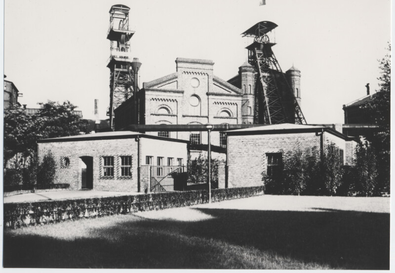 Im Vordergrund sind zwei flache, eingeschossige Gebäude zu sehen. Dahinter erhebt sich ein etwa doppelt so hohes Gebäude sowie die Fördergerüste von Schacht 3 und Schacht 4 der Zeche Consolidation im Stadtteil Gelsenkirchen-Bismarck.