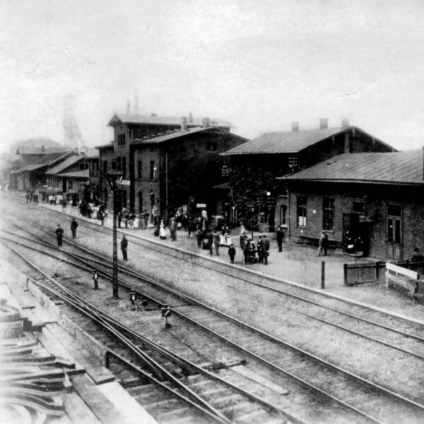 Am Gelsenkirchener Hauptbahnhof stehen um 1902 Menschen am Bahnsteig. Die Bahnhofsgebäude sind nüchterne Backsteinbauten.