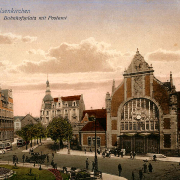 Ansicht des Gelsenkirchener Hauptbahnhofs und des Postamts nach dem Bahnhofsumbau von 1904. Beide Gebäude sind prachtvolle Jugendstilbauten. Der Vorplatz ist mit einem grünen Rondell geschmückt. Davor hält ein Auto an.