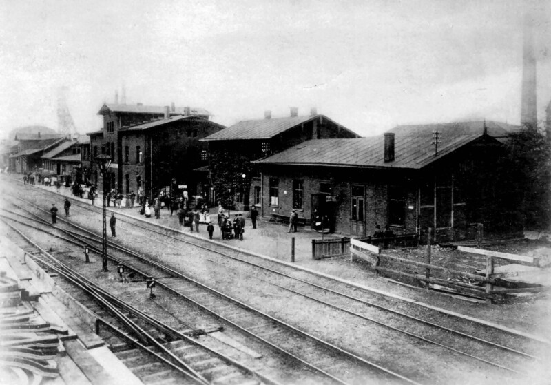 Am Gelsenkirchener Hauptbahnhof stehen um 1902 Menschen am Bahnsteig. Die Bahnhofsgebäude sind nüchterne Backsteinbauten.