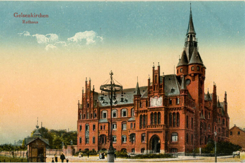 Postkartenansicht des alten Gelsenkirchener Rathauses am Machensplatz. Die Wände bestehen aus leuchtend-roten Backsteinen. Das Dach ist dunkelgrau gehalten.