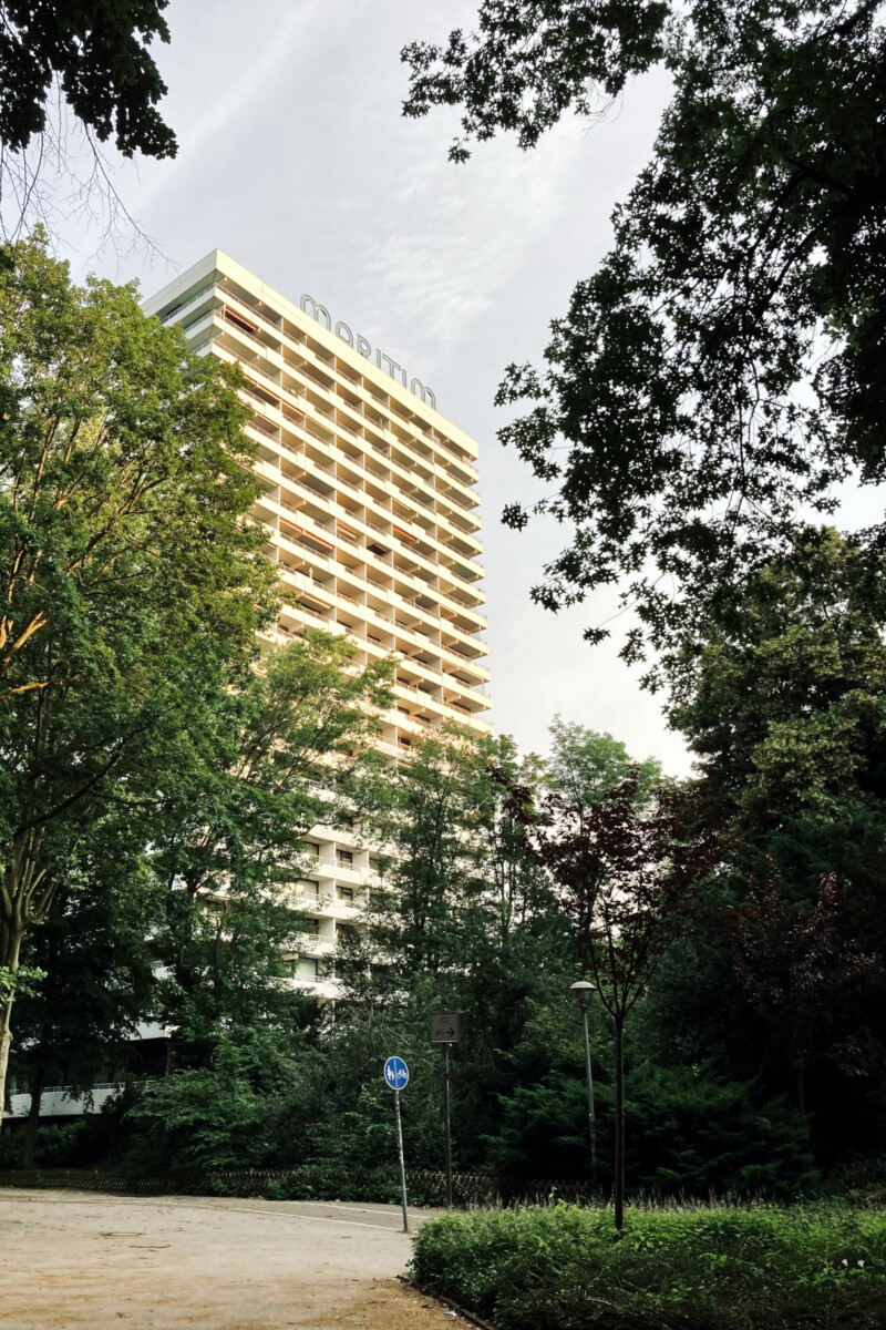 Ein weißes Hochhaus steht zwischen den Bäumen einer Parkanlagen. Auf dem Dach ist der Schriftzug "Maritim" zu sehen.