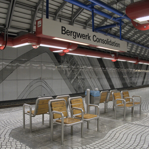 Acht Stühle stehen in der Mitte eine U-Bahnsteigs. Über ihnen hängt ein weißes Schild mit der Aufschrift "Bergwerk Consolidation".