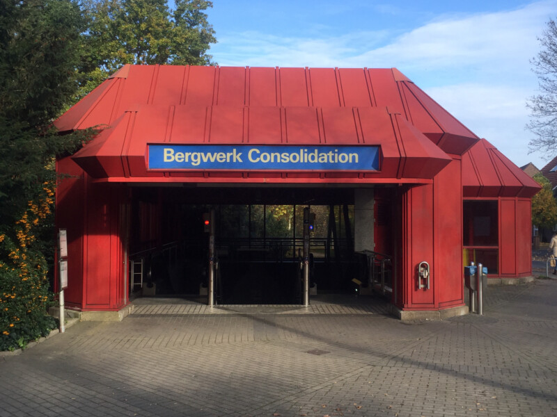 Ein rotes Eingangsgebäude zu einer U-Bahnhaltestelle. Über dem Eingang hängt ein Schild mit der Aufschrift "Bergwerk Consolidation".