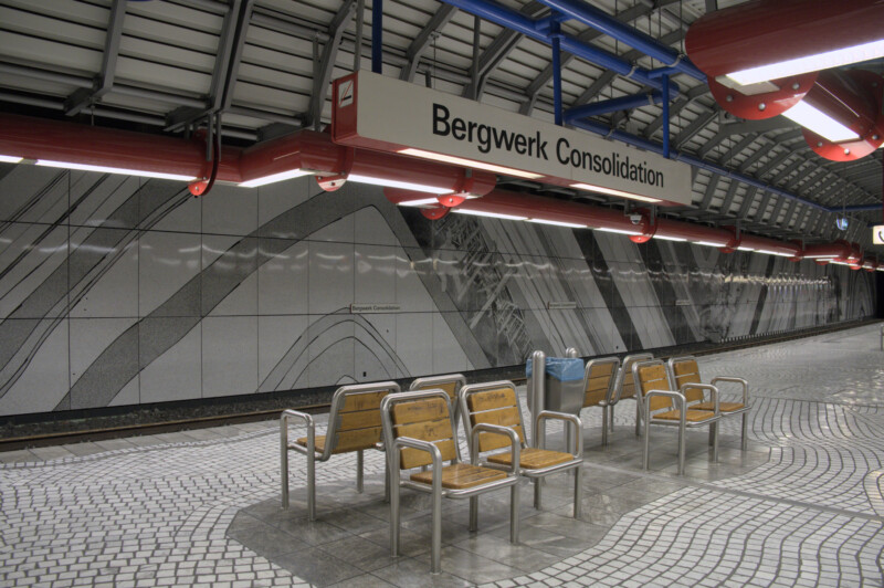 Acht Stühle stehen in der Mitte eine U-Bahnsteigs. Über ihnen hängt ein weißes Schild mit der Aufschrift "Bergwerk Consolidation".