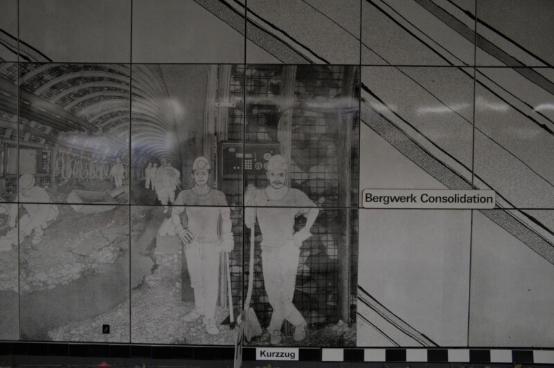 Ein Gemälde an der Wand einer U-Bahnstation zeigt Bergmänner bei der Arbeit in einem Tunnel, der sogenannten Strecke. Die zwei Arbeiter auf der rechten Bildseite blicken direkt rüber zum Betrachter.